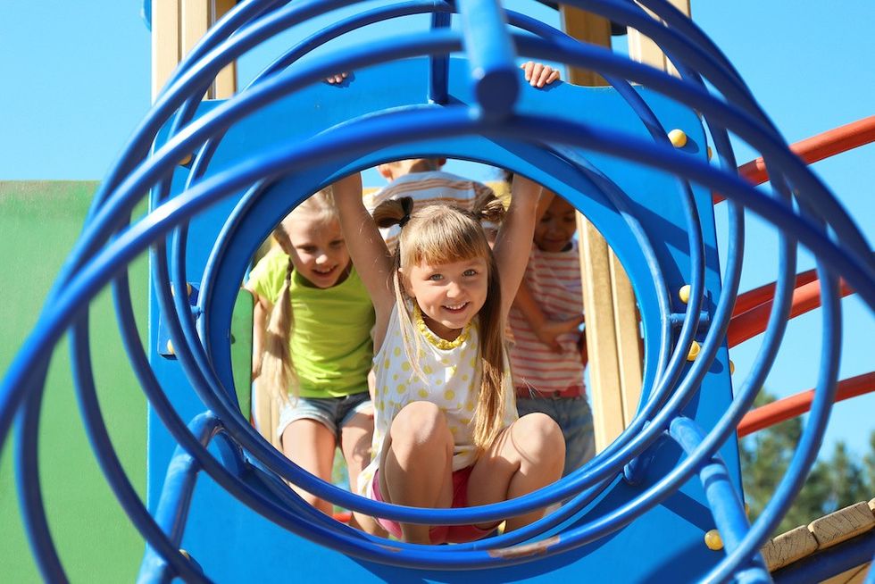 Children playing on a blue spiral playground structure, smiling and climbing.