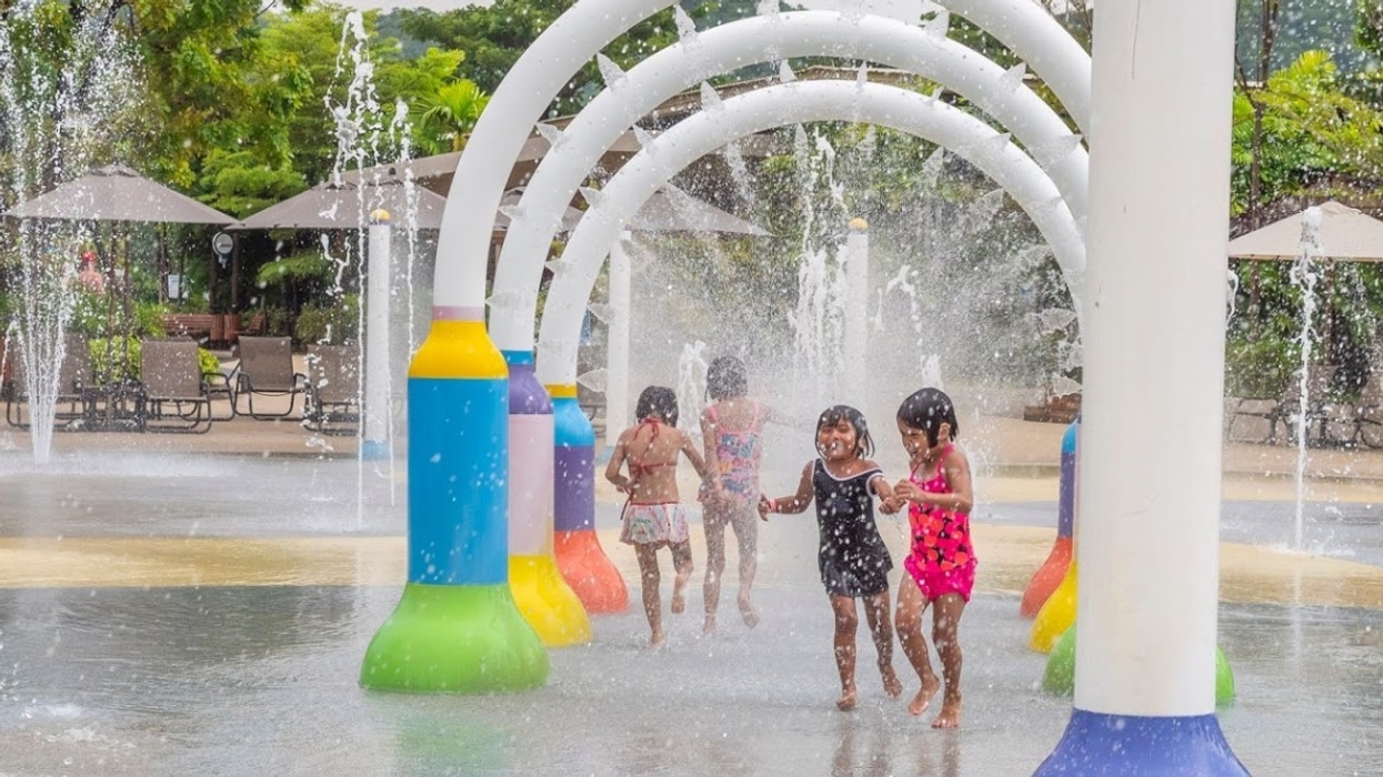 Children playing under water arches at a splash pad on a sunny day.