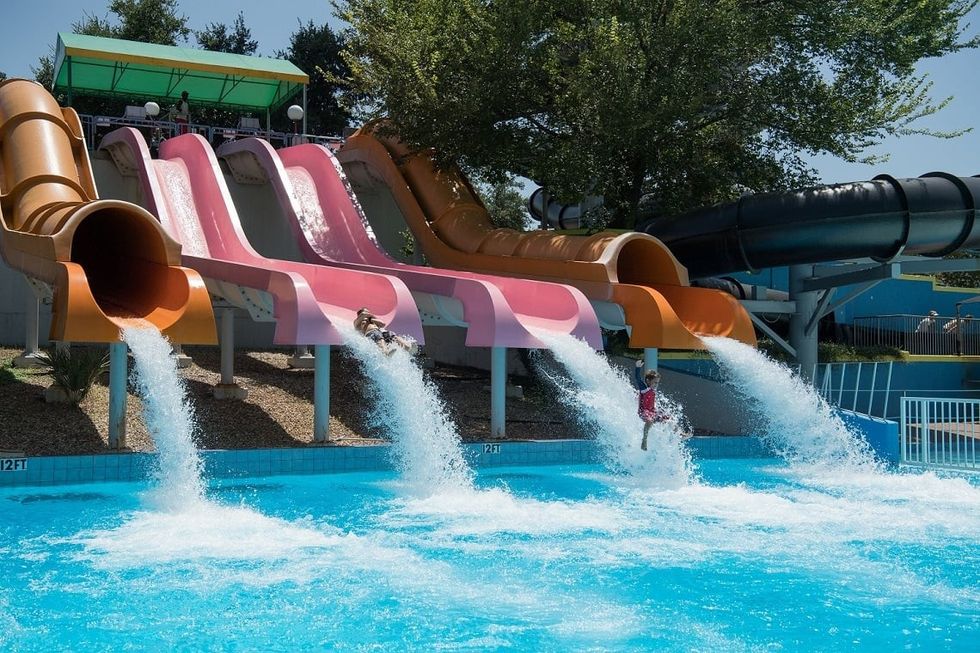 Children sliding down colorful water slides into a pool on a sunny day at Hurricane Harbor