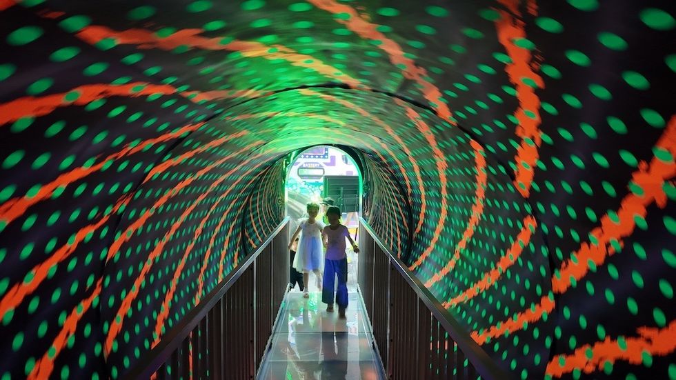 Children walking through a brightly lit, spiral-patterned tunnel.