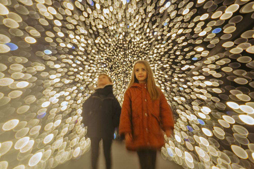 Children walking through a dazzling tunnel of blurred golden lights.
