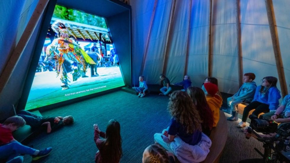 Children watching a large screen displaying a cultural dance inside a dome-shaped room at Montana Heritage Center.