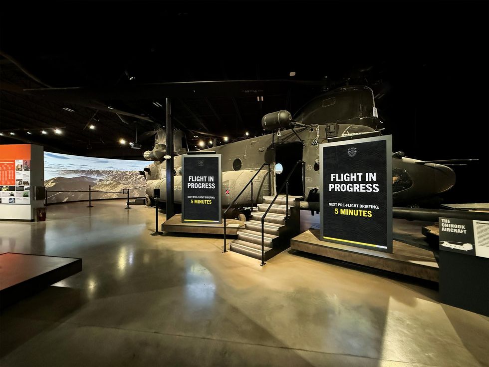 Chinook helicopter exhibit with "Flight in Progress" sign in a dimly lit museum space.