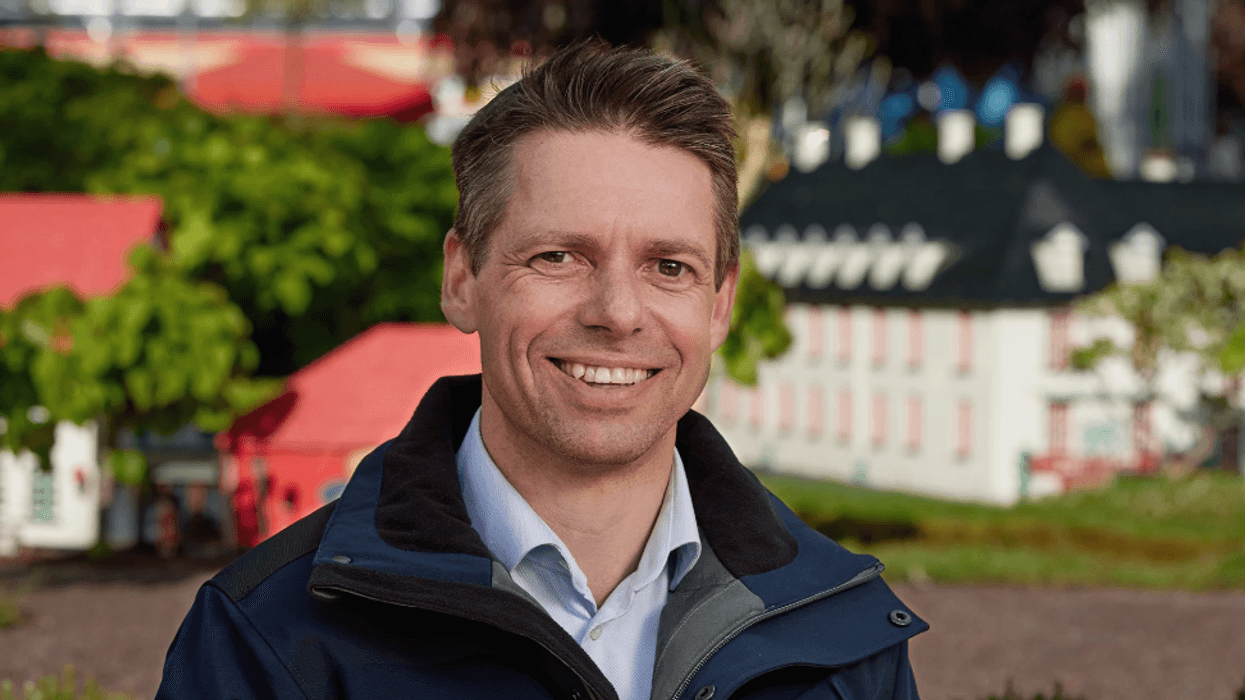 ​Christian Woller smiling outside, wearing a blue jacket, with colorful buildings in the blurred background.
