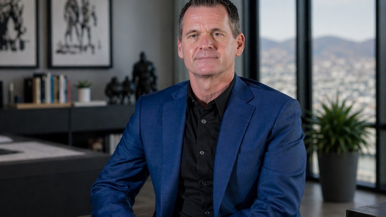 Chuck Fawcett in a blue suit sitting in a modern office with large windows and artwork.