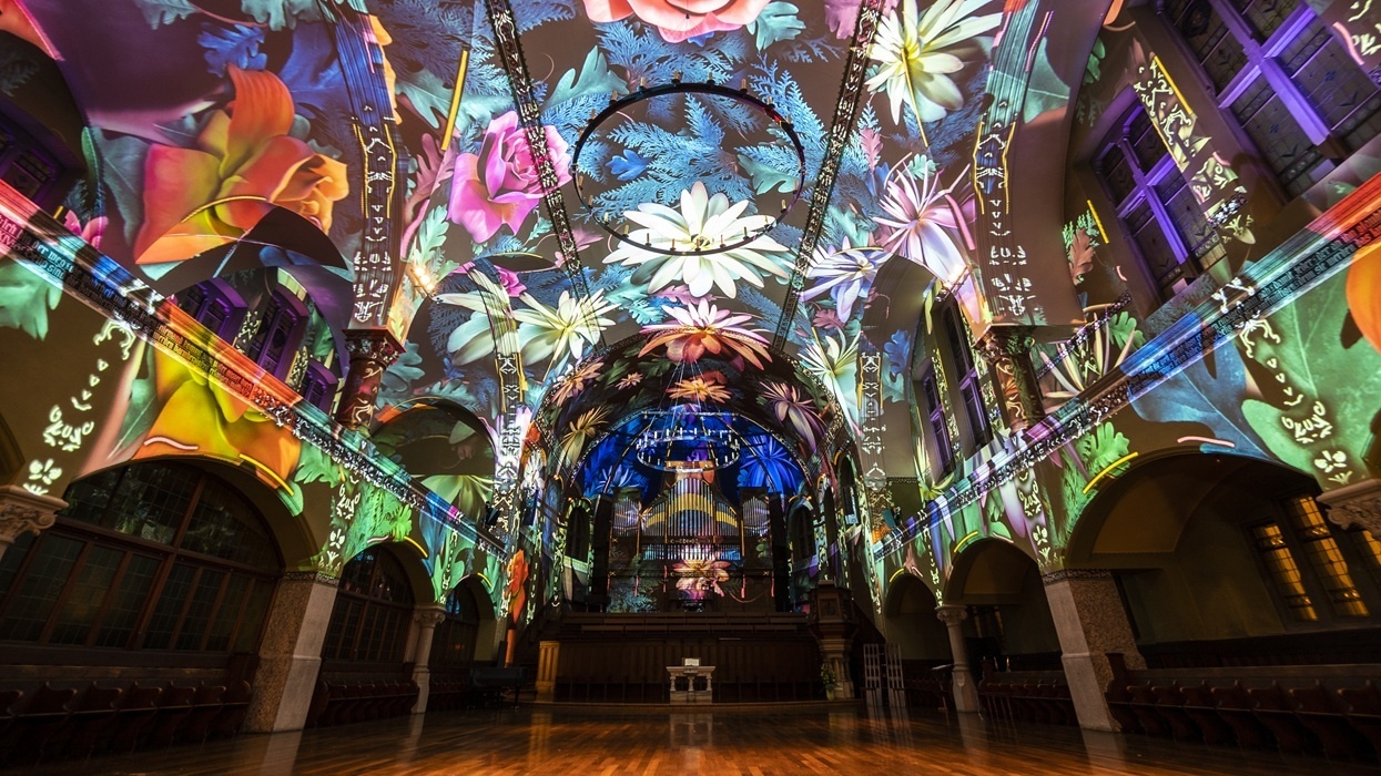 Church interior lit with colorful, vibrant floral projections on walls and ceiling.
