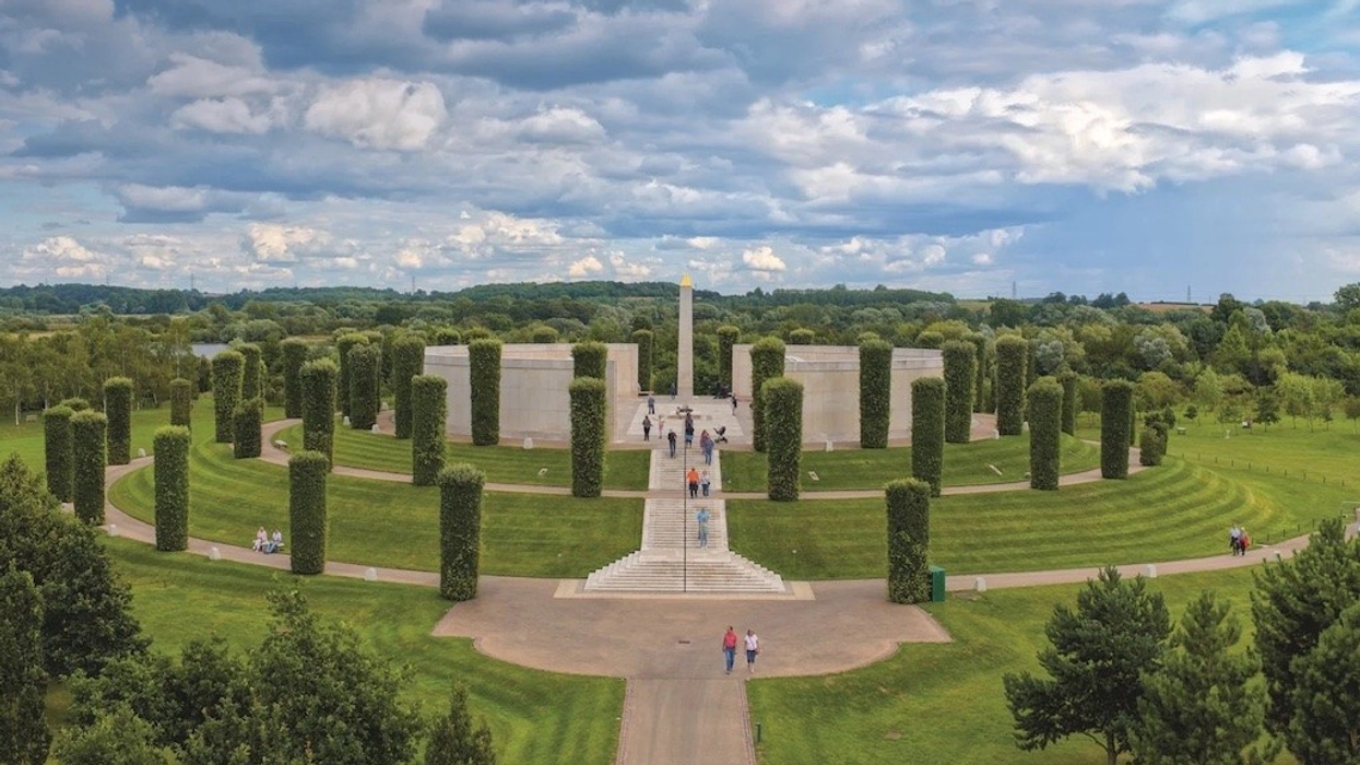 Circular memorial landscape with tall hedges, central walkway, and distant cloudy sky.