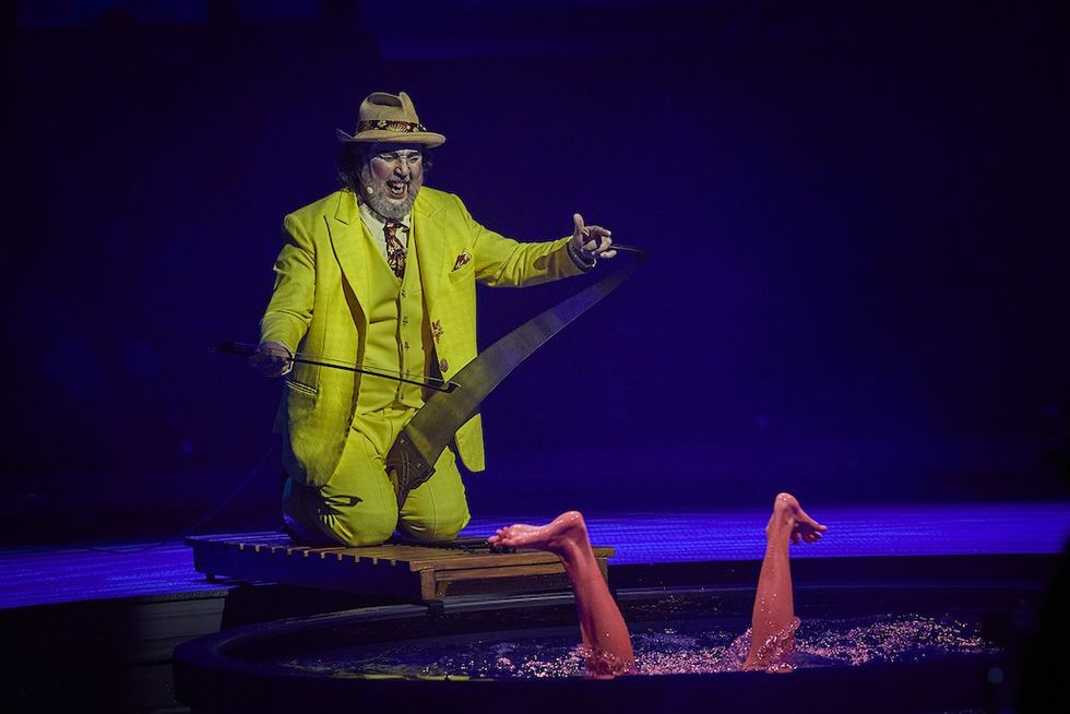 Cirque du Soleil's new show, LUD\u00d5 at BON - Performer in yellow suit plays saw while legs emerge from water ballet scene.
