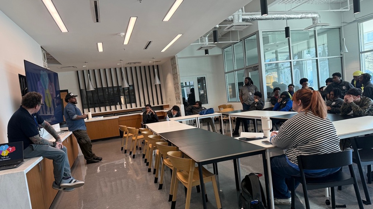 Classroom lecture with seated students and two presenters near a large screen.