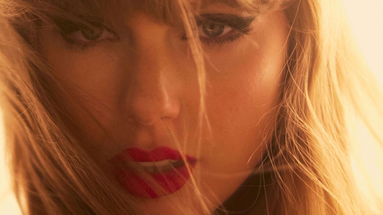 Close-up of Taylor Swift with windblown hair, red lipstick, and intense eye makeup.