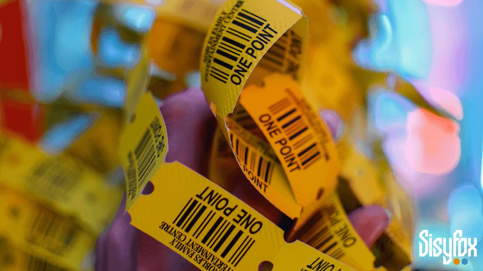 Close-up of yellow arcade tickets labeled "One Point" with a colorful blurred background.