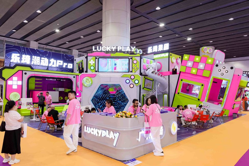 Colorful arcade booth at GTI China Expo with people in pink uniforms and a "LUCKYPLAY" sign above.
