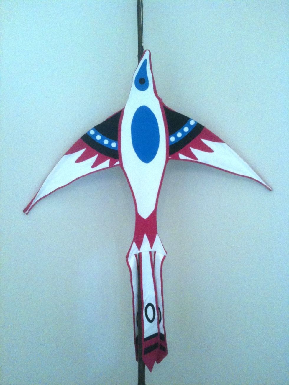 Colorful bird-shaped kite with red, blue, and black patterns hanging indoors.