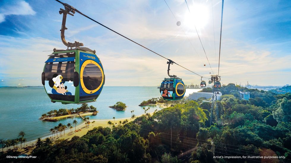 Colorful cable cars with Disney images above tropical landscape and ocean.