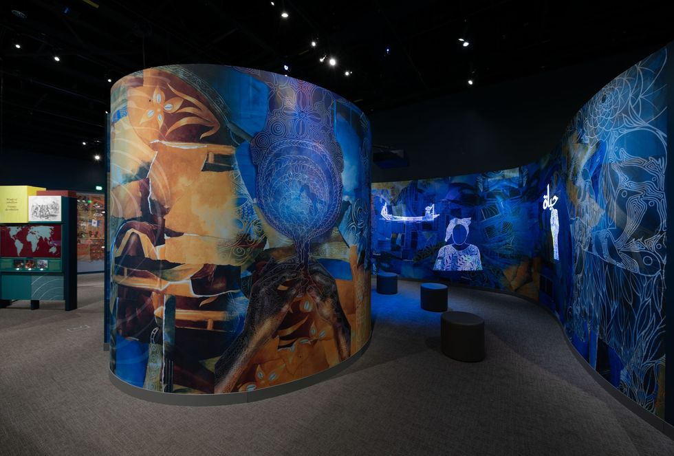 Colorful curved mural with abstract and human figures in a dimly lit exhibition space.