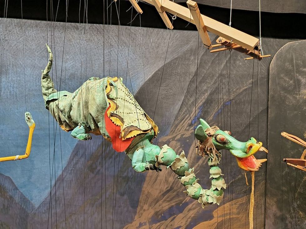 Colorful dragon marionette against a scenic backdrop, controlled by wooden strings.