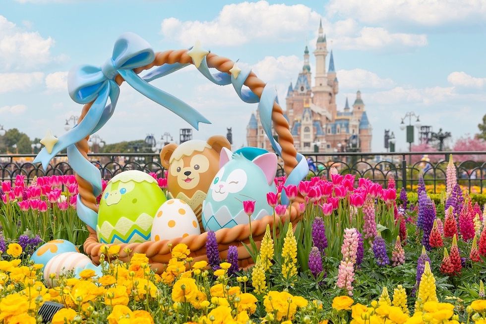 Colorful Easter eggs in a basket with a castle backdrop, surrounded by vibrant flowers.
