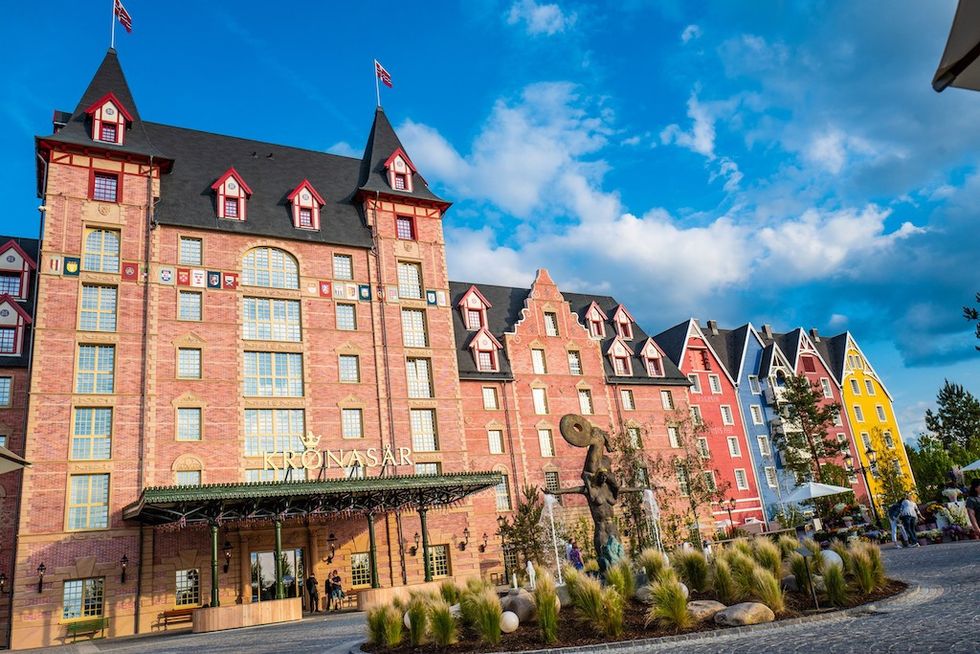 Colorful, European-style hotel, Kr\u00f8nas\u00e5r Hotel at Europa-Park, under a vibrant blue sky with fluffy clouds.