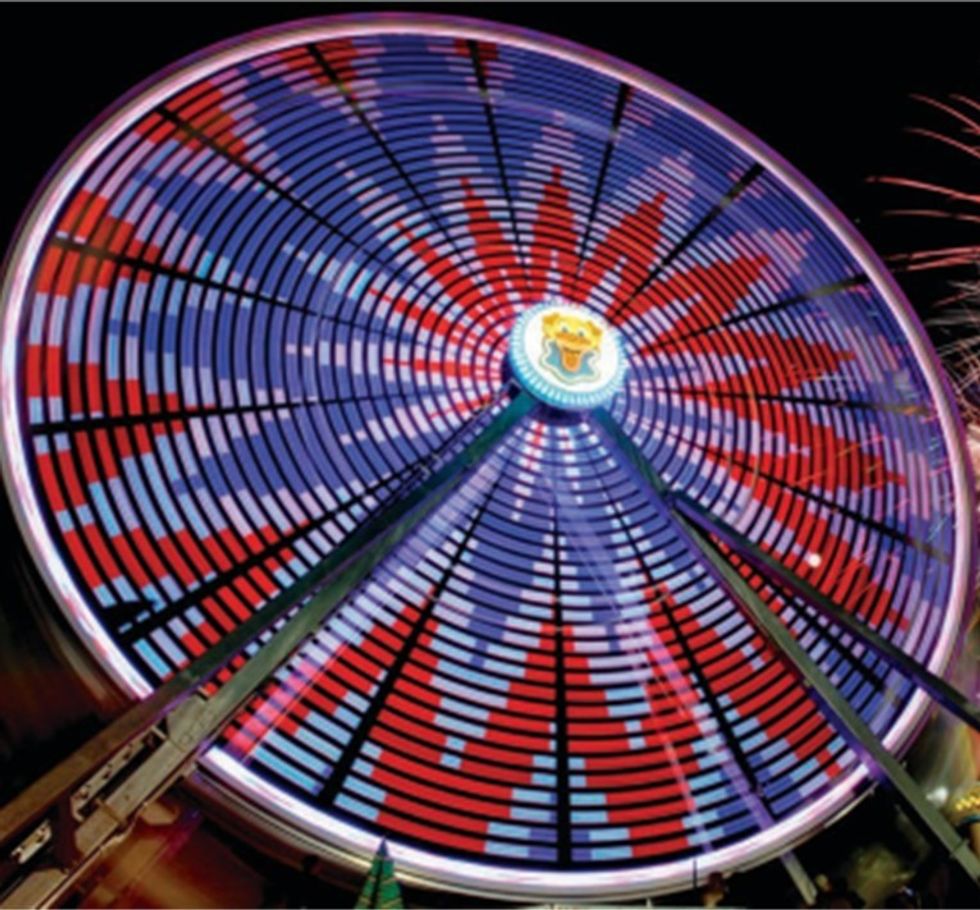 Colorful Ferris wheel at night with vivid red and blue lights in a striped pattern.