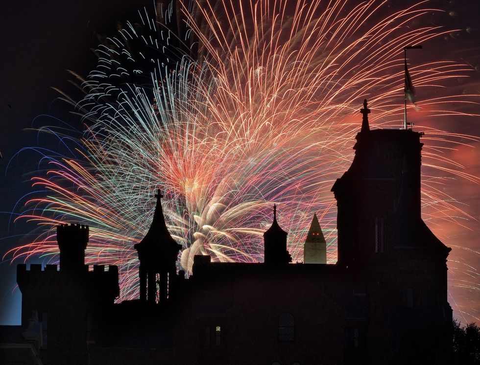 Colorful fireworks burst over a silhouetted castle-like building called the Smithsonian Castle at night.