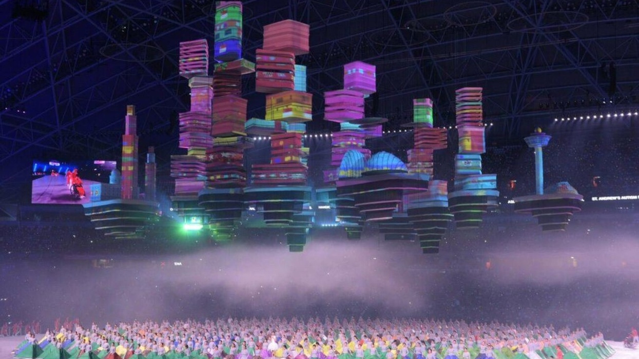 Colorful, floating structures over a performing crowd in a stadium event.