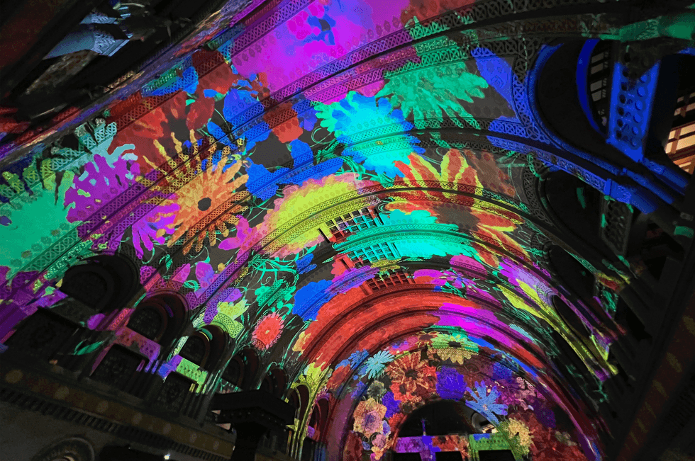 Colorful floral light projections on an ornate arched ceiling.
