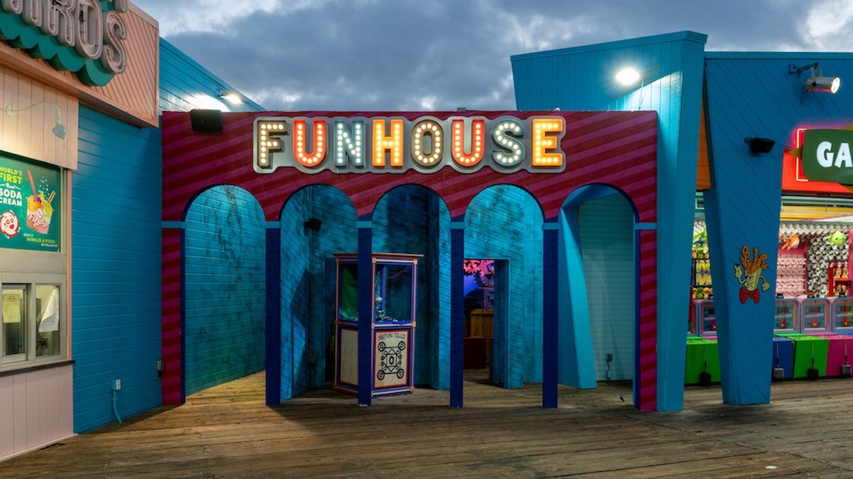 Colorful funhouse entrance on a boardwalk under a cloudy sky.