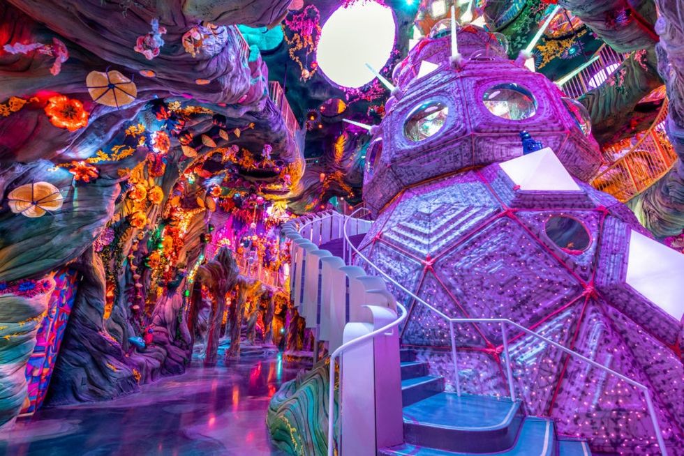 Colorful, futuristic indoor exhibit with vibrant lights, plants, and geometric structures.