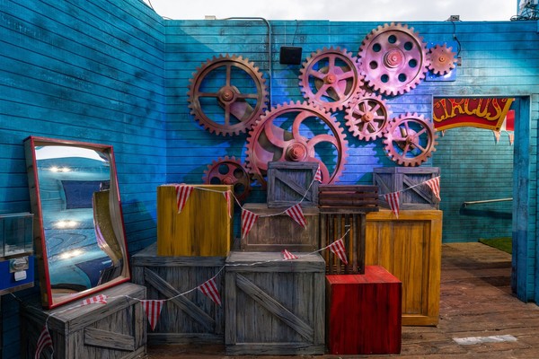 Colorful gears and crates with a circus theme against a blue wooden wall.