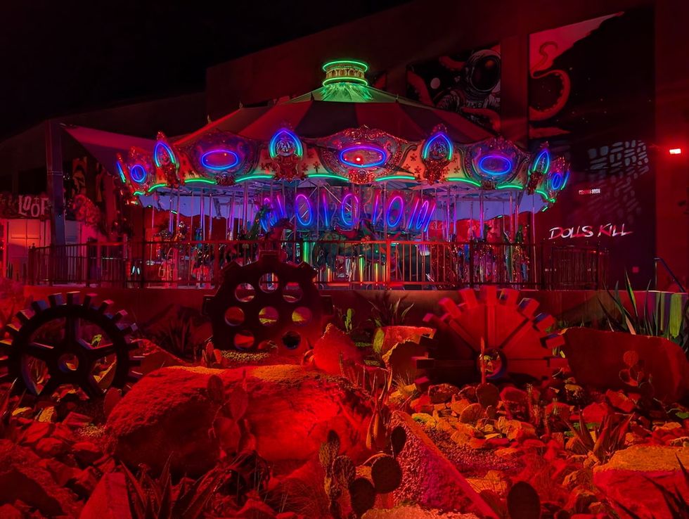Colorful illuminated carousel with red lighting and gears in foreground at night.