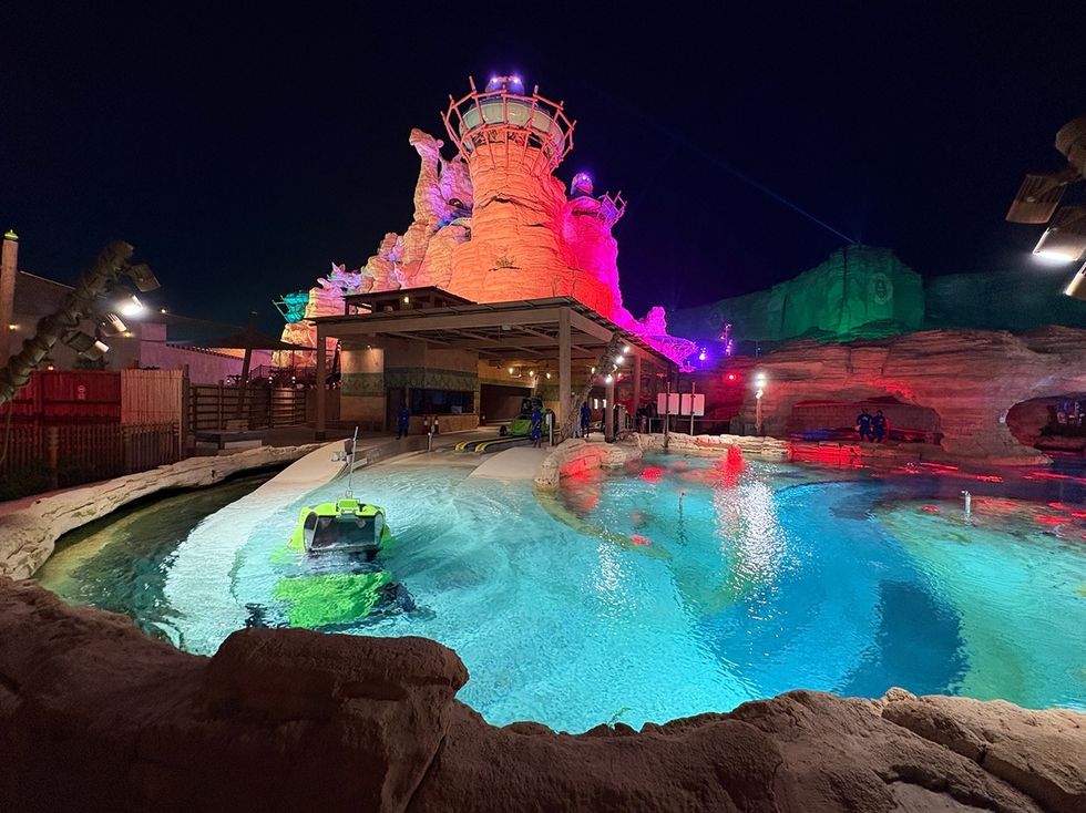 Colorful, illuminated rocks and pool at a nighttime amusement park scene.
