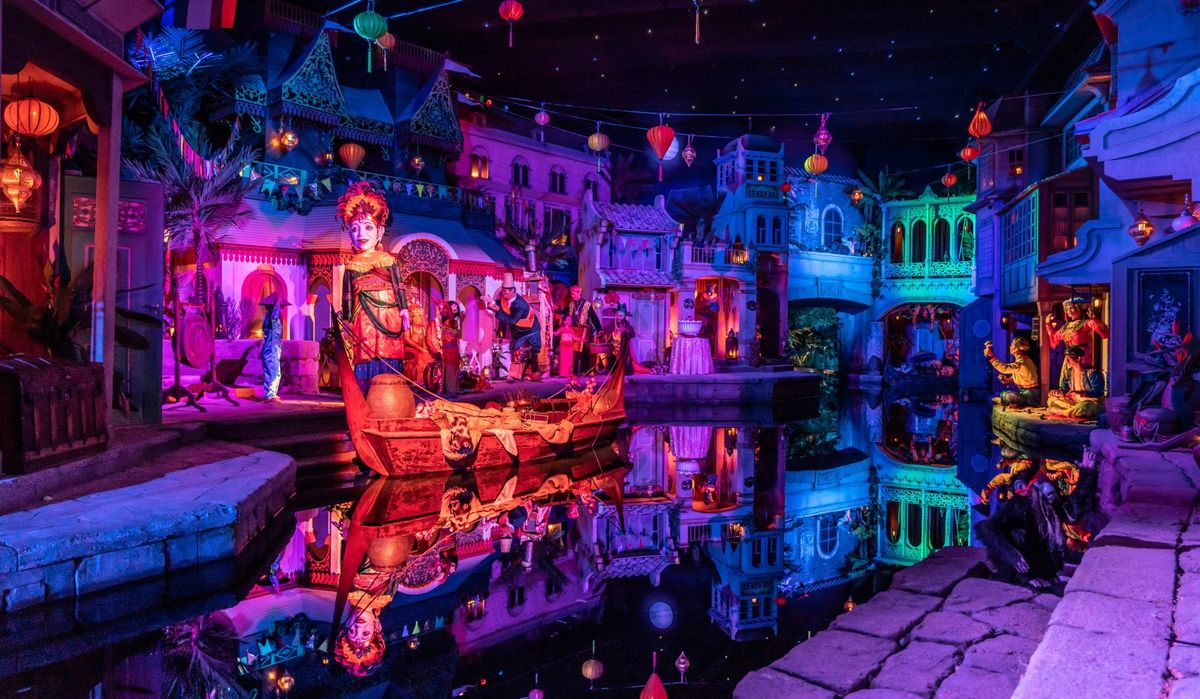 Colorful illuminated scene with intricate statues and reflections on a canal at night.