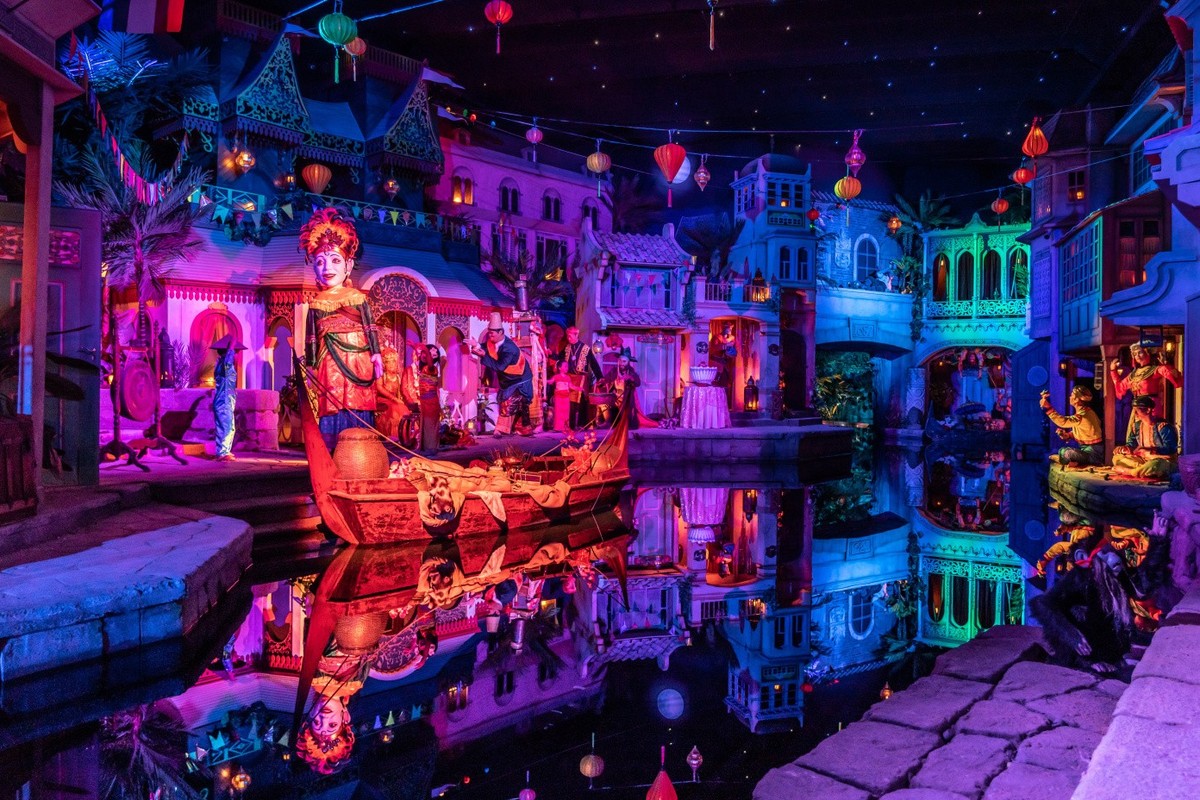 Colorful illuminated scene with intricate statues and reflections on a canal at night.
