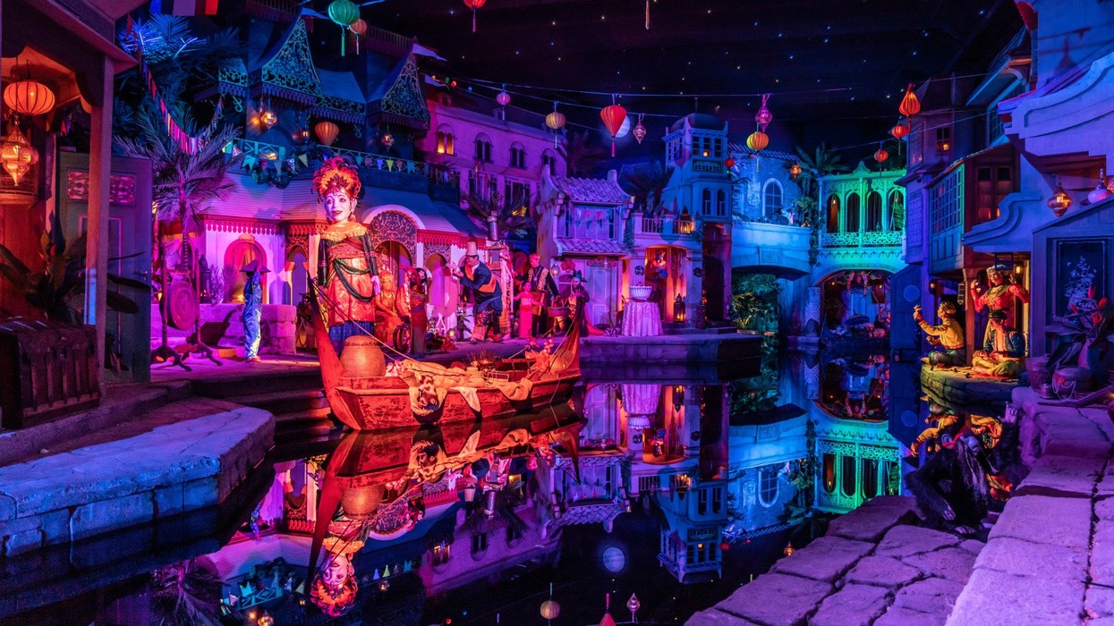 Colorful illuminated scene with intricate statues and reflections on a canal at night.