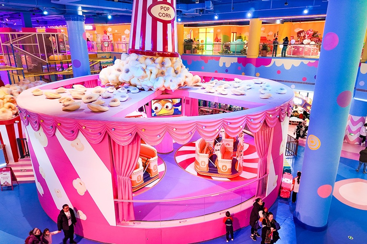 Colorful indoor amusement park with a popcorn-themed attraction and visitors walking around.