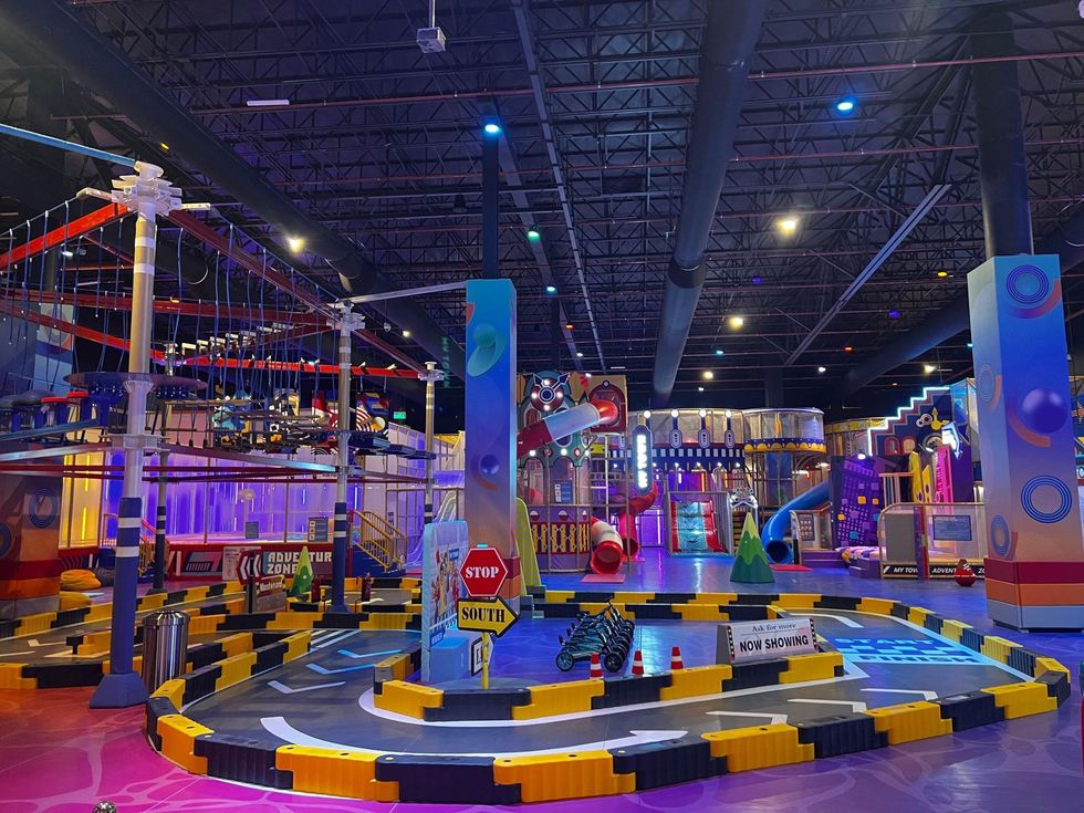 Colorful indoor amusement park with slides, rope course, and vibrant lighting.