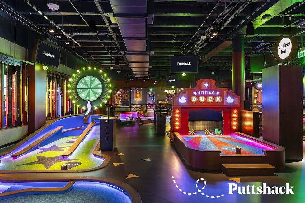 Colorful indoor mini-golf course with neon lights and a prize wheel.