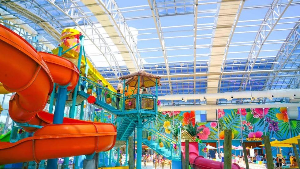Colorful indoor water park with slides, tropical decor, and a glass ceiling.