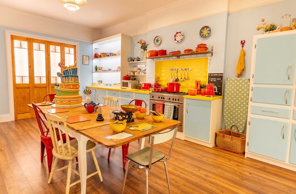 Colorful kitchen with a large cake, vintage decor, and vibrant utensils on a wooden table.