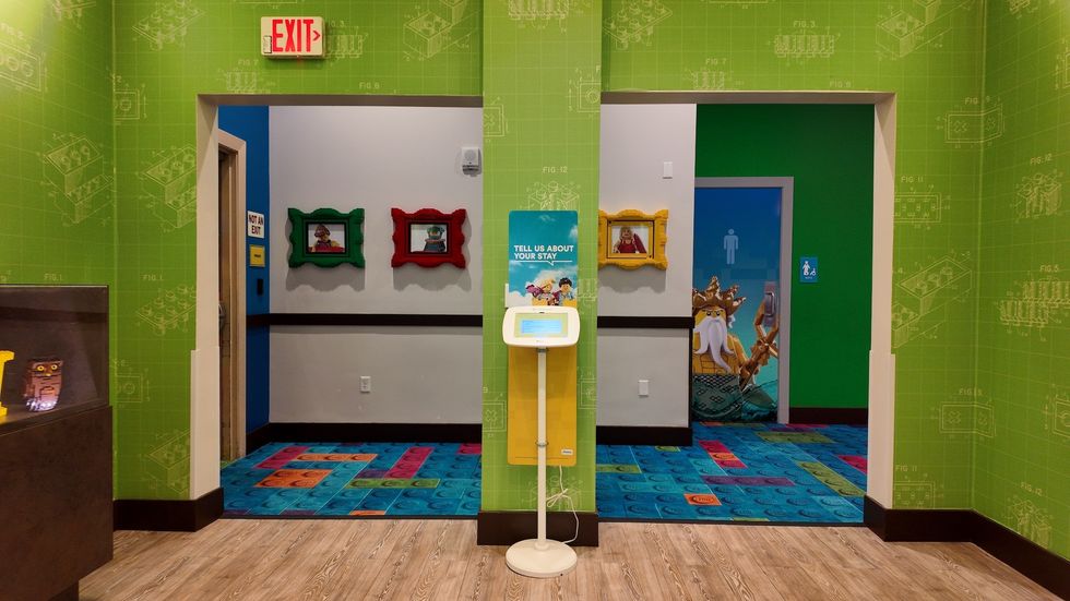 Colorful LEGO-themed hallway with two doorways, exit sign, and interactive kiosk.