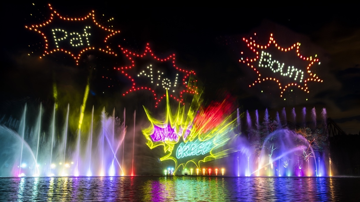 Colorful light show with comic words "Paf," "Aïe," "Boum," and "CRAC" above illuminated fountains at at Parc Astérix.