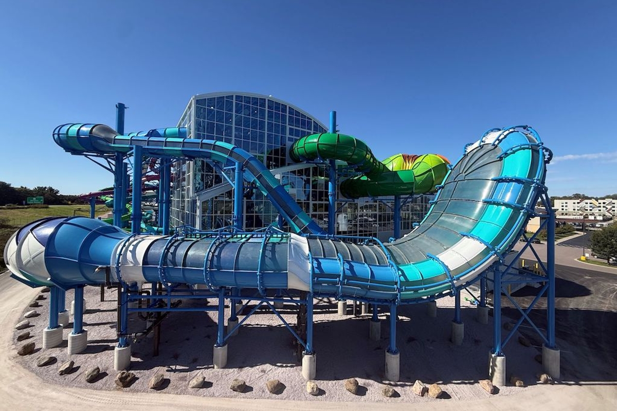 Colorful, looping water slide structure outside a large glass building under a clear blue sky.