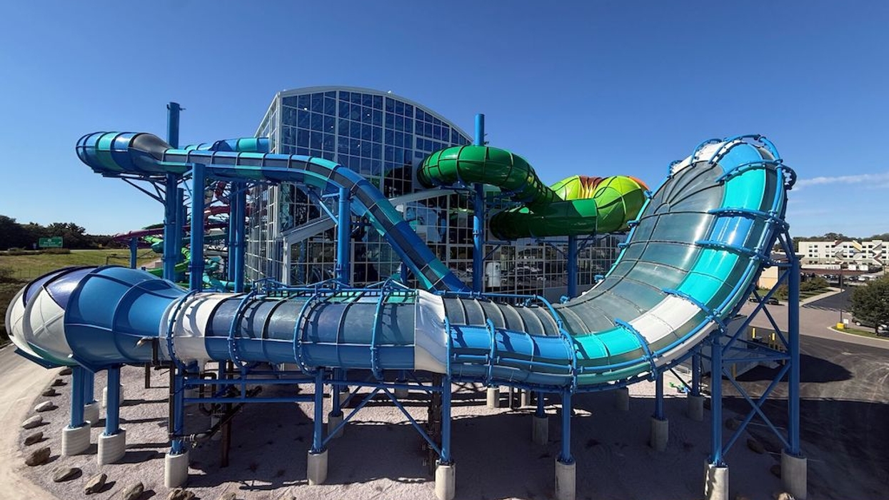 Colorful, looping water slide structure outside a large glass building under a clear blue sky.