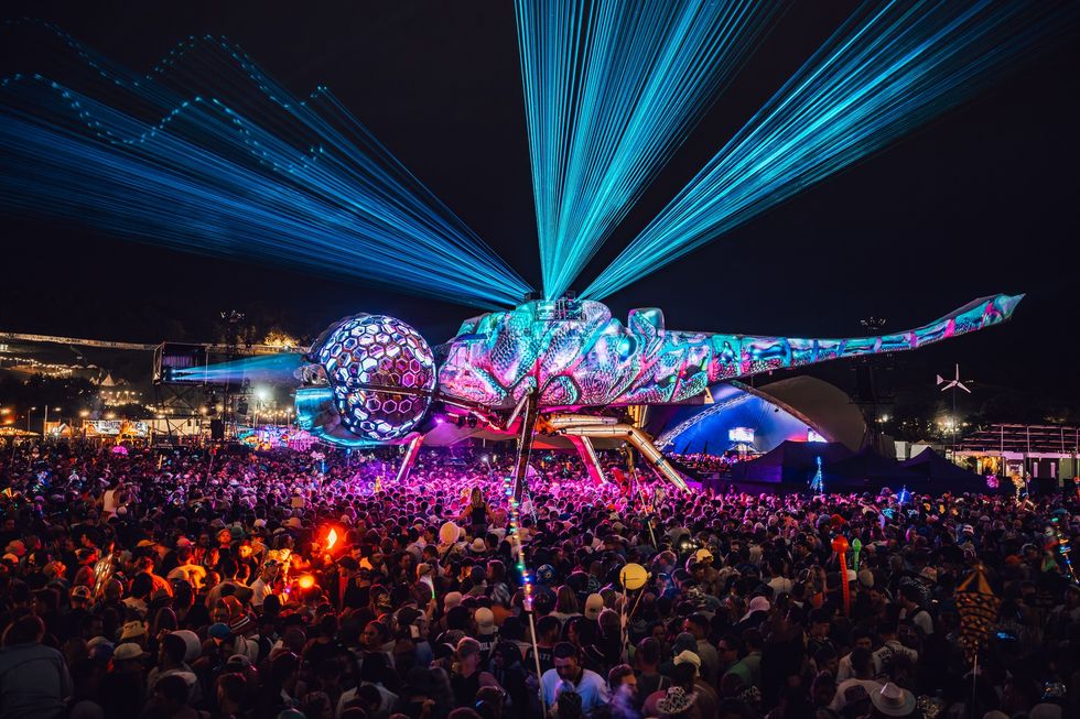 Colorful mechanical insect with laser lights above a crowded night festival.