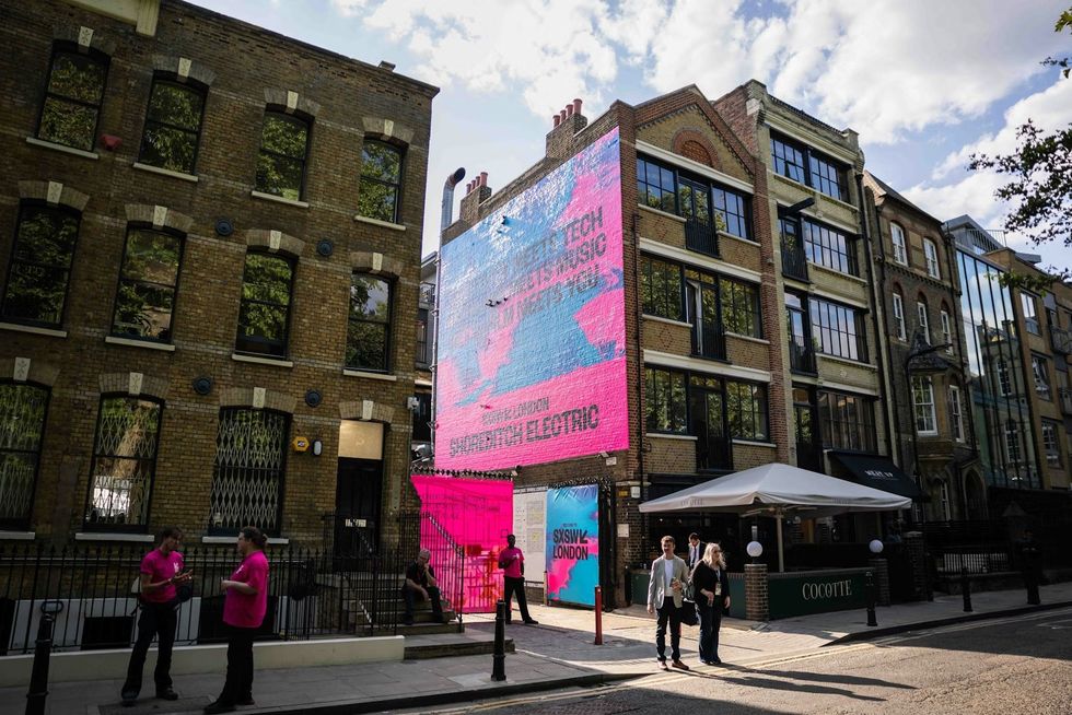Colorful mural with text on brick building, people chatting, and outdoor seating below at SXSW London