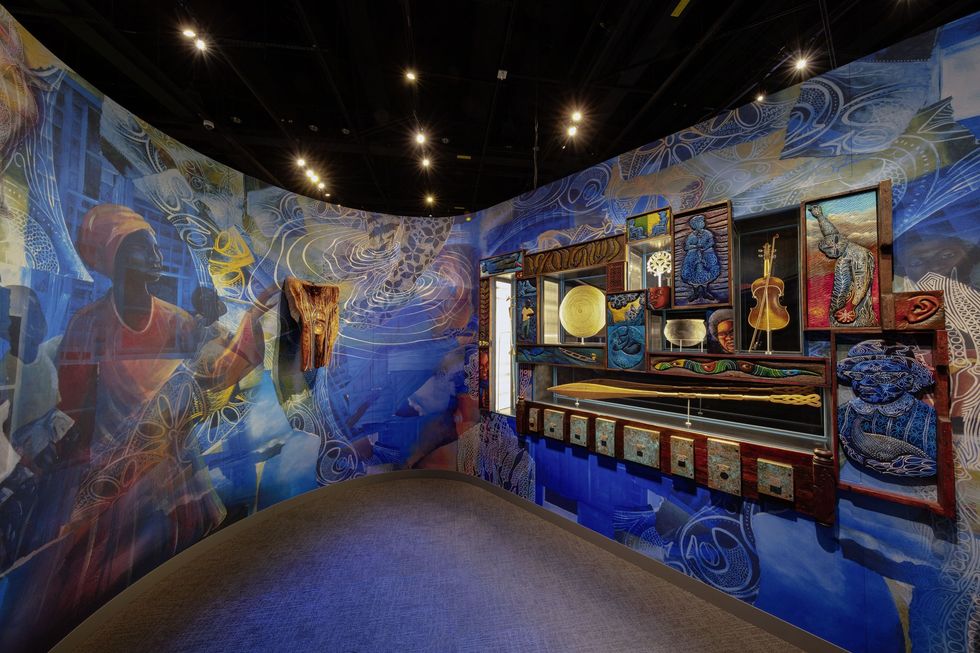 Colorful museum display with African art and musical instruments on blue, mural-covered walls.