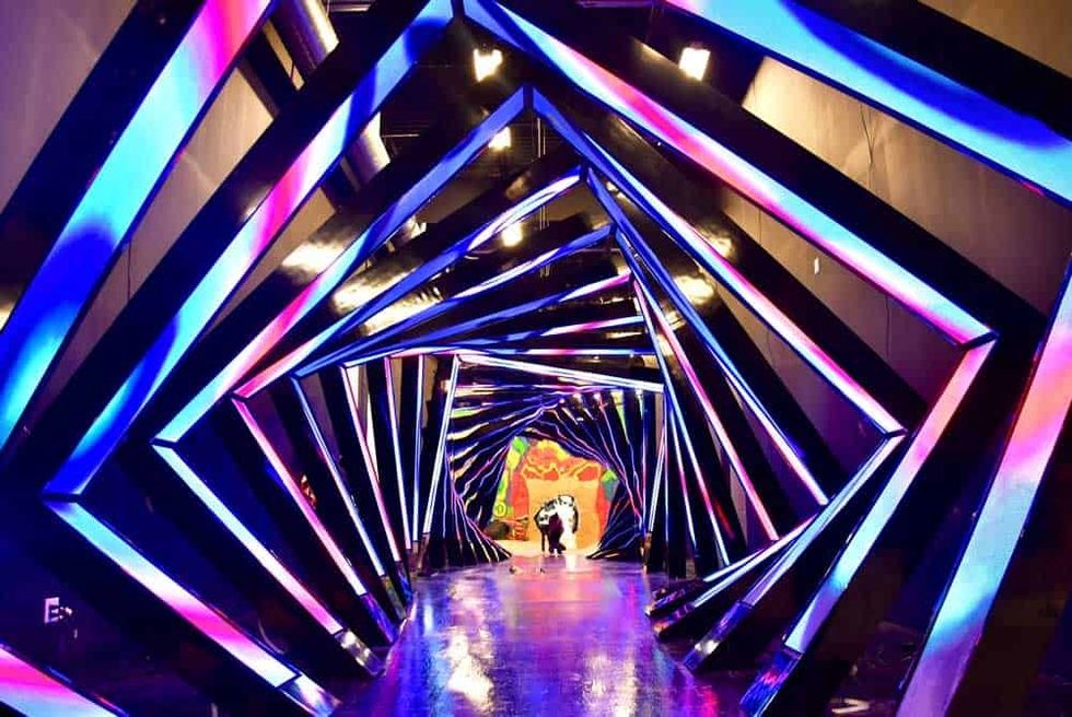 Colorful neon-lit tunnel with geometric patterns and a vibrant mural at the end at Seismique