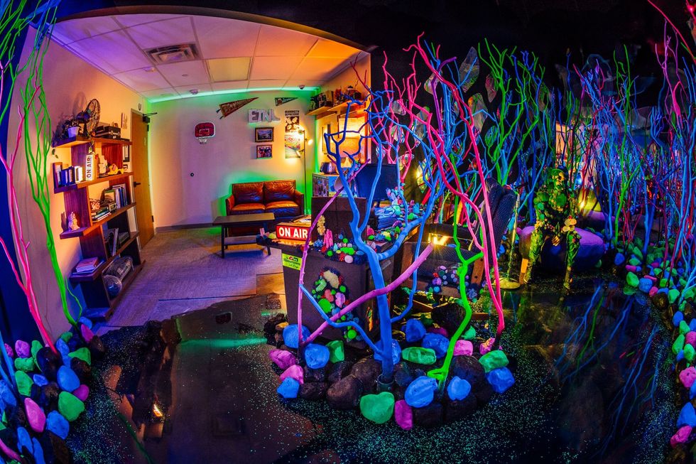 Colorful neon room with vibrant painted branches, glowing stones, and "ON AIR" sign at Meow Wolf Radio Tave