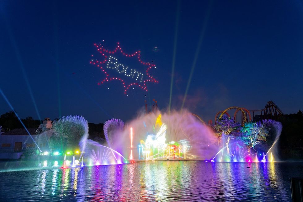Colorful night fountain show with lights and "Boum" in drones above.