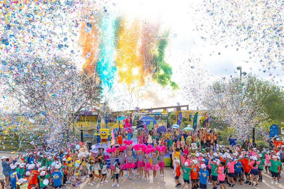 Colorful parade at Universal Kids Resort with confetti, crowds in vibrant attire, and cartoon character mascots celebrating.